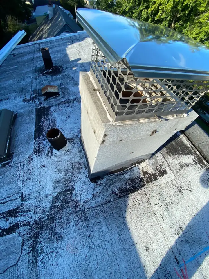 A chimney with a mesh cap and vent pipes on a flat roof